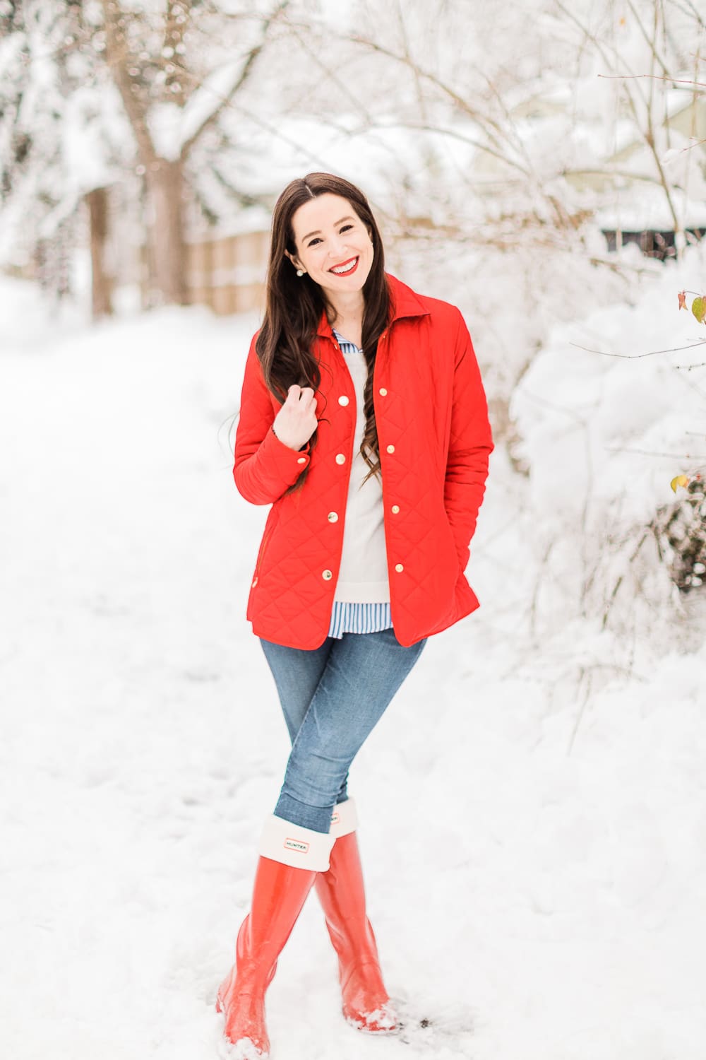 Preppy Winter Outfit: Red Quilted Jacket with Matching Red Hunter Boots by affordable fashion blogger Stephanie Ziajka from Diary of a Debutante, how to style red Hunter boots with tall welly boot socks, how to style a red quilted jacket, red quilted jacket styled with red tall Hunter boots, Hunter tall welly boot socks, a blue striped oxford, white crewneck sweater, and skinny jeans