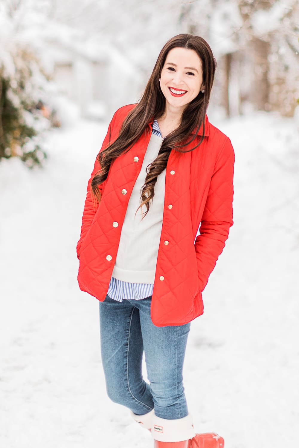 Preppy Winter Outfit: Red Quilted Jacket with Matching Red Hunter Boots by affordable fashion blogger Stephanie Ziajka from Diary of a Debutante, how to style red Hunter boots with tall welly boot socks, how to style a red quilted jacket, red quilted jacket styled with red tall Hunter boots, Hunter tall welly boot socks, a blue striped oxford, white crewneck sweater, and skinny jeans