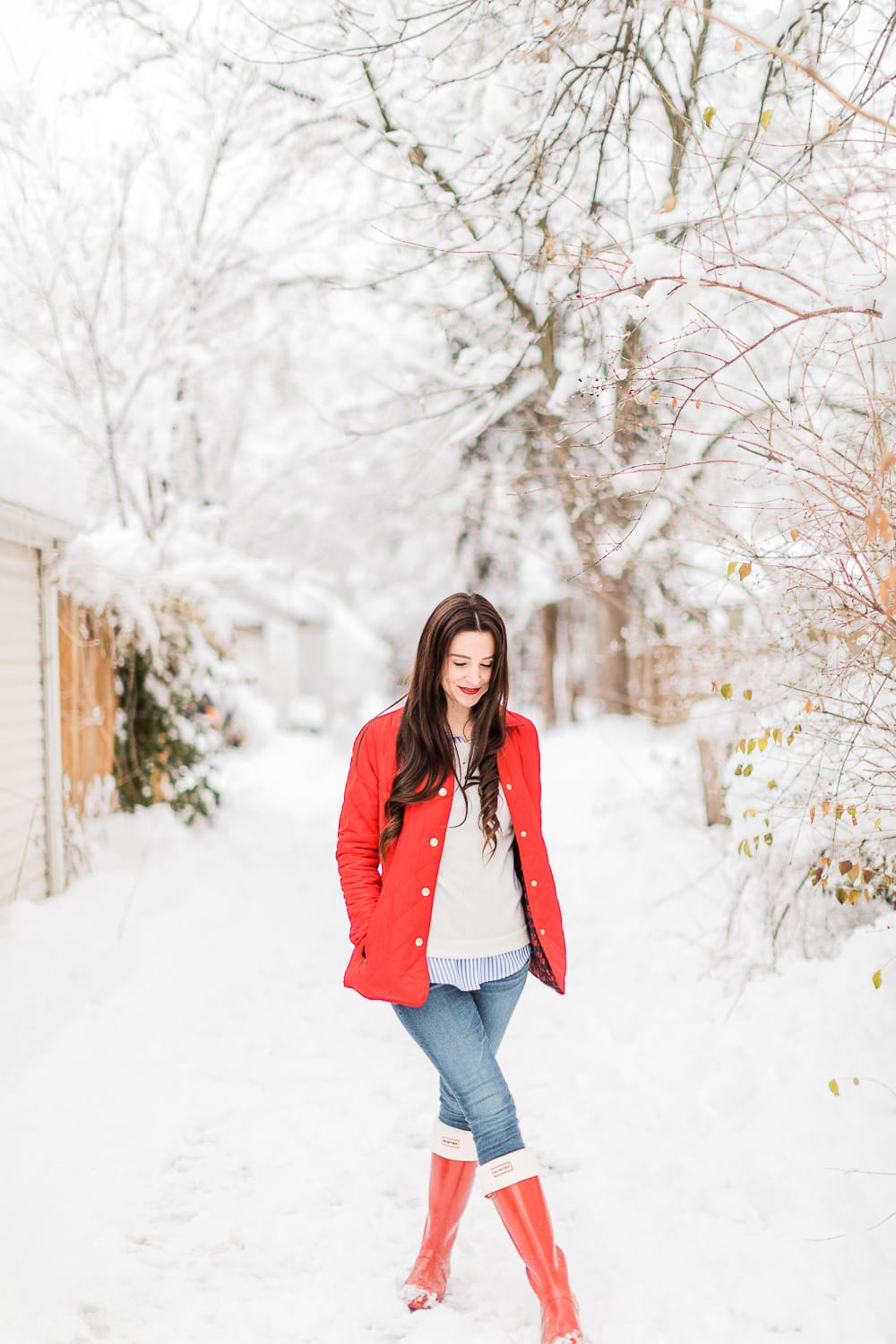 Preppy Winter Outfit: Red Quilted Jacket with Matching Red Hunter Boots by affordable fashion blogger Stephanie Ziajka from Diary of a Debutante, how to style red Hunter boots with tall welly boot socks, how to style a red quilted jacket, red quilted jacket styled with red tall Hunter boots, Hunter tall welly boot socks, a blue striped oxford, white crewneck sweater, and skinny jeans
