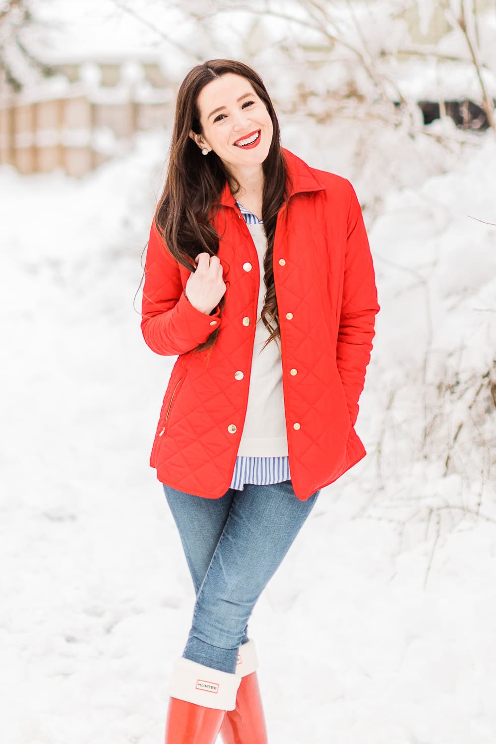 Preppy Winter Outfit: Red Quilted Jacket with Matching Red Hunter Boots by affordable fashion blogger Stephanie Ziajka from Diary of a Debutante, how to style red Hunter boots with tall welly boot socks, how to style a red quilted jacket, red quilted jacket styled with red tall Hunter boots, Hunter tall welly boot socks, a blue striped oxford, white crewneck sweater, and skinny jeans